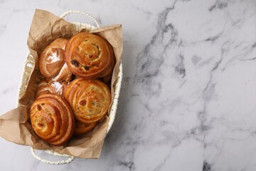 Delicious rolls with raisins and sugar powder in basket on white marble table, top view with space...