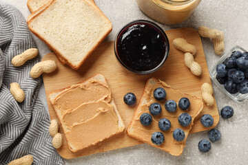 Tasty peanut butter sandwiches with fresh blueberries jam and peanuts on gray table, flat lay