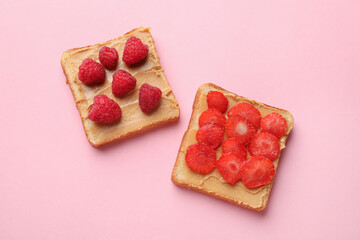Tasty peanut butter sandwiches with fresh berries on pink background, flat lay
