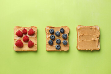 Tasty peanut butter sandwiches with fresh berries on light green background, flat lay