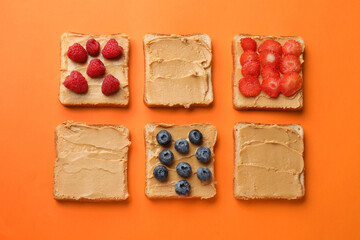 Tasty peanut butter sandwiches with fresh berries on orange background, flat lay