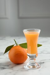 Delicious tangerine liqueur in shot glass and fresh fruit on white marble table