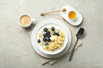 Tasty oatmeal with banana, blueberries, butter and milk served in bowl on light grey table, flat lay