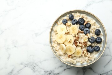 Tasty oatmeal with banana, blueberries, walnuts and milk served in bowl on white marble table, top view. Space for text