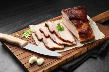 Pieces of baked pork belly served with parsley and garlic on black textured table