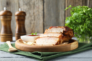 Pieces of baked pork belly served with sauce on grey wooden table
