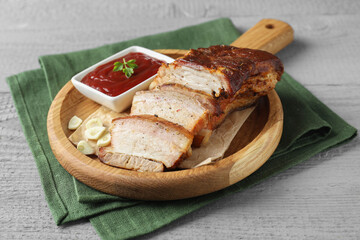 Pieces of baked pork belly served with sauce on grey wooden table