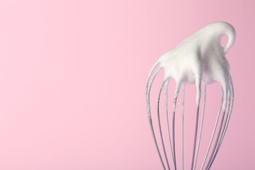 Whisk with whipped egg whites on pink background, closeup