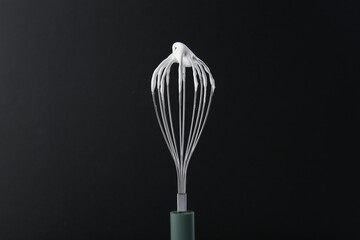 Whisk with whipped cream on black background
