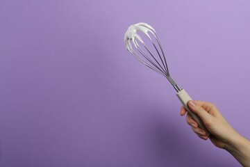 Woman holding whisk with whipped cream on violet background, closeup. Space for text