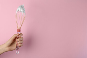 Woman holding whisk with whipped cream on pink background, closeup. Space for text