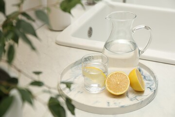 Jug, glass with clear water and lemons on white table in kitchen