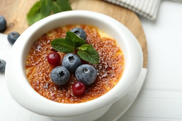 Delicious creme brulee with berries and mint in bowl on white table, closeup