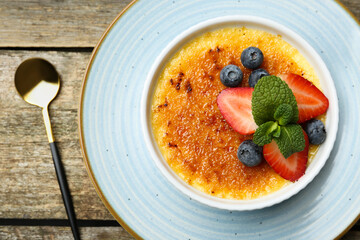 Delicious creme brulee with berries and mint in bowl served on wooden table, top view