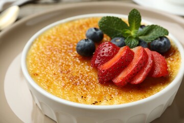 Delicious creme brulee with berries and mint in bowl on plate, closeup