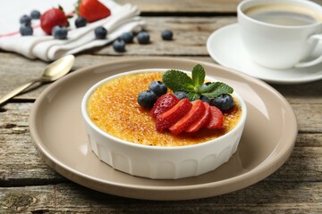 Delicious creme brulee with berries and mint in bowl on wooden table, closeup