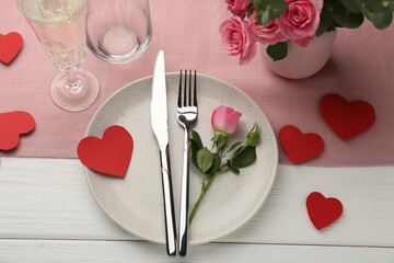 Romantic place setting with flowers and red paper hearts on white wooden table, above view. St. Valentine's day dinner