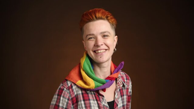 A woman with a bright orange quiff exudes warmth and LGBTQ pride, her plaid shirt and multicolored scarf complement the friendly ambiance. Camera 8K RAW.