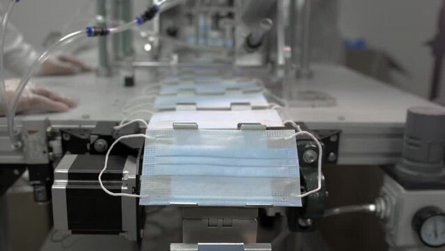 Production of disposable medical clothing for protection against the virus. Medical mask on conveyor belt in the workshop of factory for production of clothing. Manufacture of masks. Slow motion