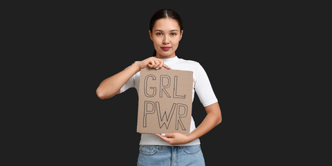 Young woman holding paper with slogan GRL PWR on dark background. Feminism concept