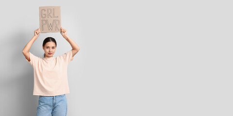 Young woman holding paper with slogan GRL PWR on light background with space for text. Feminism...