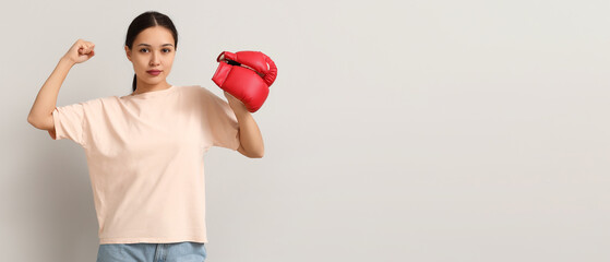 Young woman with boxing gloves flexing muscles on light background with space for text. Feminism...