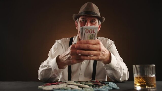 With a triumphant smile, a man in a fedora receives and joyfully counts a hefty sum of cash at the poker table, savoring the sweet taste of his win. High quality 4k footage