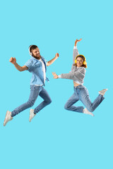 Happy couple in love with headphones jumping on blue background