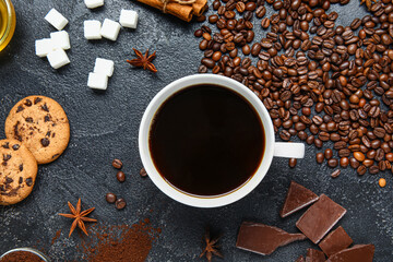 Cup of tasty coffee with cinnamon, chocolate, cookies and sugar on black background