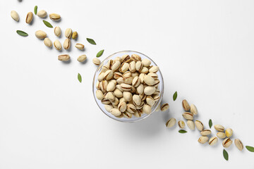 Glass bowl with tasty pistachio nuts and leaves on white background
