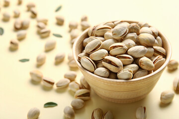 Bowl with tasty pistachio nuts and leaves on yellow background