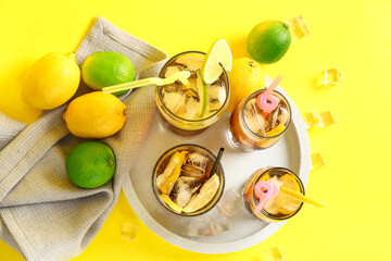 Board with glasses of tasty Long Island iced tea, ice cubes and citrus fruits on yellow background