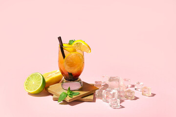 Glass of tasty Long Island iced tea, citrus fruits and ice cubes on pink background