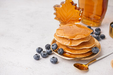 Plate of tasty pancakes with blueberries and maple syrup on white background