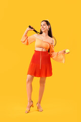 Stylish young woman with tennis racket and ball on yellow background