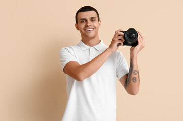 Male photographer with modern camera on beige background