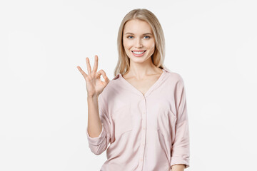 Young blonde woman in casual showing OK gesture and looking at camera isolated on white background....
