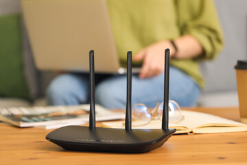 Modern wi-fi router on table of woman with laptop at home, closeup