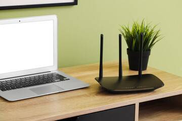 Modern wi-fi router with laptop on table near green wall in office
