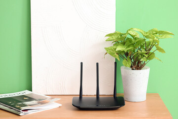 Modern wi-fi router with plant, magazines and painting on shelf near green wall