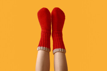 Legs of young woman in warm red knitted socks on yellow background