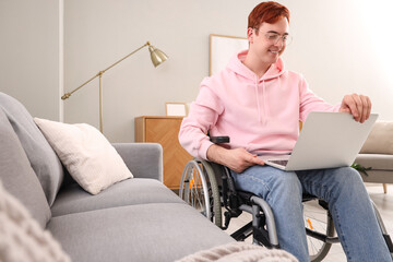 Fototapeta premium Young man in wheelchair with laptop at home