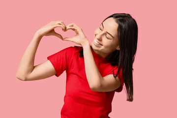 Beautiful young woman making heart with hands on pink background