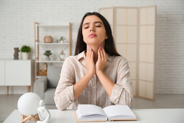 Young woman with book suffering from thyroid gland problem at home