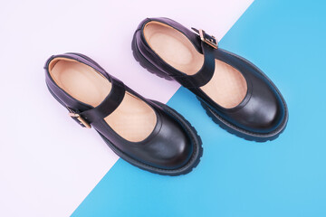 Pair of female black leather shoes on pink and blue background close-up top view.
