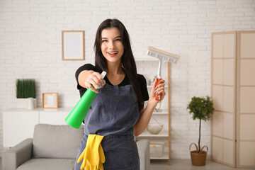 Young woman with squeegee and detergent in living room
