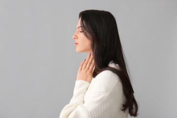 Young woman with thyroid gland problem on grey background