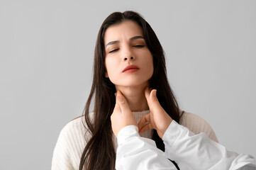 Endocrinologist examining thyroid gland of young woman on grey background