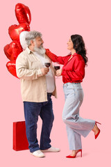 Beautiful mature couple with heart-shaped balloons and glasses of wine on pink background. Valentine's Day celebration