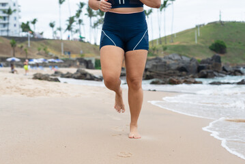 Legs of a young fitness woman running on the beach sand towards the camera.